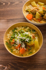 Chicken soup with vegetables in a deep bowl on a wooden table.