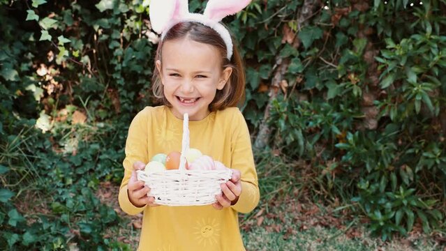 Easter egg hunt. Excited emotion surprise adorable child girl in bunny ears rabbit costume hold basket with Easter colored eggs. Children positive emotions. Kid happy Easter. Egg hunting outside