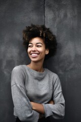 shot of a happy young woman standing against a grey wall outside