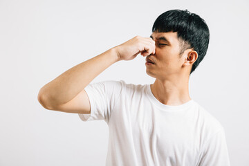 A disgusted Asian man holds his nose, expressing strong displeasure due to a bad smell situation....
