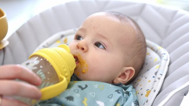 Baby drinking water from the bottle with a straw during feeding