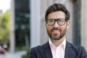 Confident mature businessman with beard smiling in front of office building, corporate leader portrait