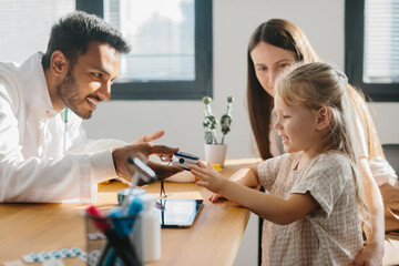 Fototapeta premium A young pediatrician measures the pulse of a small patient. A mother with a preschool-aged daughter at a doctor's appointment.
