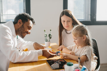 Obraz premium A young pediatrician measures the pulse of a small patient. A mother with a preschool-aged daughter at a doctor's appointment.