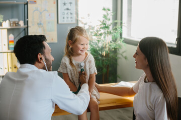 Mother and child seeing family practitioner. Smiling pediatrician with stethoscope checking little girl's lungs.