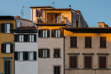 Traditional street houses of Florence with shabby yellow walls and brown and green shutters on the...