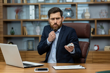 A serious-looking adult male working busily at a desk in a disorganized home office, dressed in a formal suit.