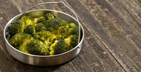 Steamed broccoli in a stainless steel steamer on a rustic wooden table. Healthy vegetable concept. Copy space.