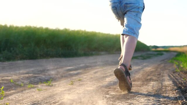 Male feet of small boy wearing sandals running on trail across field. Happy child jogging on meadow rejoicing summertime. Kid having fun in rural environment. Summer or childhood concept. Slow motion