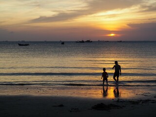 Panoramic sunset on the beach with silhouettes of a father and a child, fiery sky background