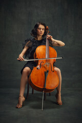 Fototapeta na wymiar Beautiful young woman, cellist sitting with cello on vintage green background. Magazine cover about talented musicians in the classical music scene. Concept of classical art, retro style, music