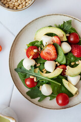 Salad with strawberries, awokado,
pine nuts and arugula on a white plate. Plate of salad on white background