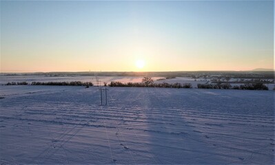 the sun rising behind a hill on the horizon, with snow all around