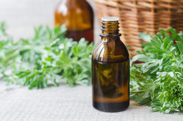 Small bottle with essential wormwood oil (extract, tincture, infusion). Old wooden background. Aromatherapy, spa and herbal medicine concept. Copy space.