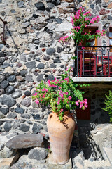 Beautiful vintage balcony with colorful flowers, terracotta pot, red chairs and natural stone wall in a narrow street of Pyrgos Kallistis village, Santorini. Greek Islands, European Vacation.  - obrazy, fototapety, plakaty