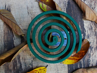 Top view of a mosquito coil on the holder on the wooden, board with some withered leaves. 