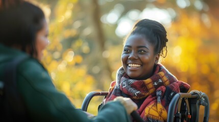 Young cheerful caucasian caregiver and african american woman in wheelchair outdoors smiling and talking to each other - obrazy, fototapety, plakaty
