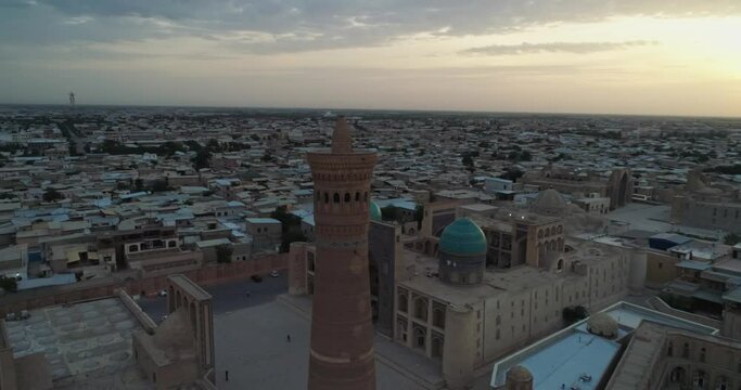 The drone flies around the minaret of the architectural complex Poi-Kalon. In the background are the old houses of Bukhara, Uzbekistan. Early cloudy morning