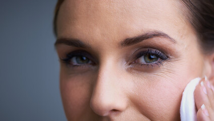 Naklejka premium Woman, eyes and pad for makeup, beauty or removal in anti aging or cosmetics on a gray studio background. Closeup of female person wiping face with cotton in satisfaction for collagen or cleaning