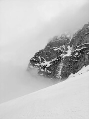 Grayscale vertical shot of a rocky mountain in the fog in snowy weather