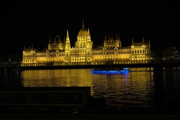 Obraz premium Illuminated Hungarian Parliament Building and a nearby boat at night in Budapest, Hungary