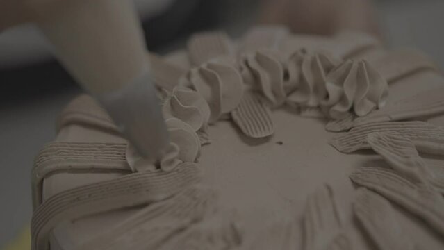 Close-up view of decorating a cake with chocolate custard from a piping bag