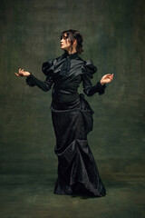 Woman in Victorian style black dress, standing in a dramatic pose against dark vintage green...