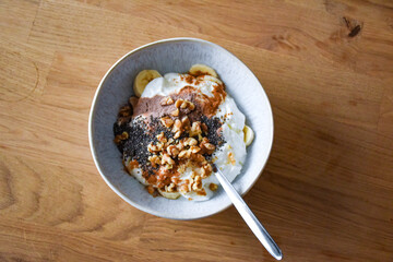 Breakfast bowl with yogurt, banana, chocolate protein, walnuts and chia seeds in a ceramic bowl