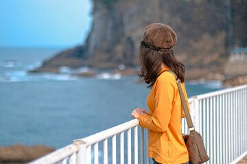 秋の海を眺めるオレンジ色のスウェットシャツを着た女性