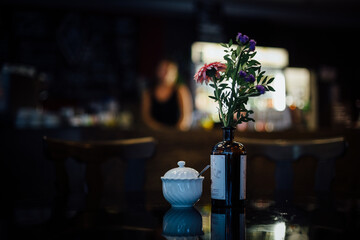 Vase mit Blumen in Cafe mit Frau unscharf im Hintergrund theke
