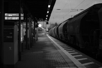 Urban train station scene featuring a stationary train, standing next to a pedestrian sidewalk