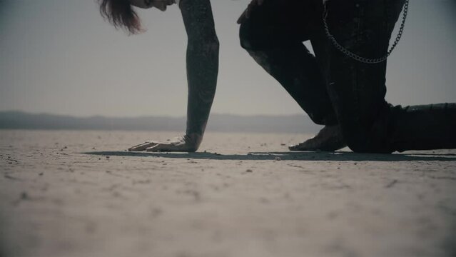 Never give up. Exhausted barefoot man walking through desert in pain and falls on his knee. Guy gets up and keep walking. Cinematic shot in slow motion. Dry lake. Cold color correction, 4k