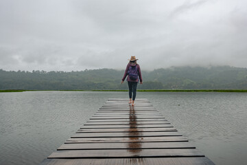 Traveler woman walks along a pier in a lagoon in the Peruvian jungle.