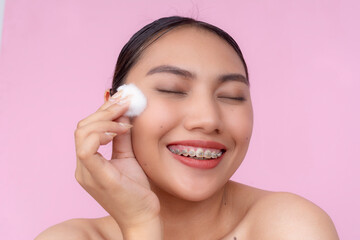 A young Asian woman feeling refreshed after using a cotton ball to apply toner or astringent on her...