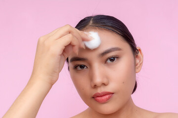 A pensive young Asian woman using a cotton ball to apply toner or astringent on her forehead....
