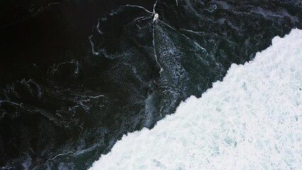 Aerial slow-motion view of foamy waves covering a dark sandy coastline