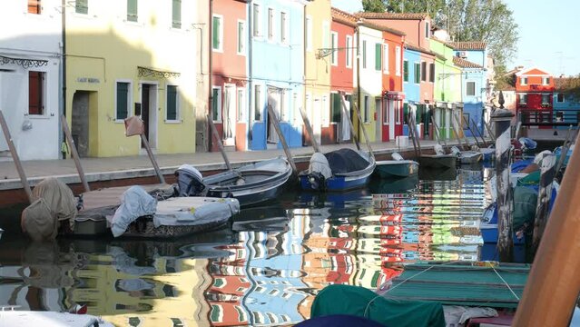 Colorful Houses with moored boats reflections on the water of the canal in Burano, Venezia island city