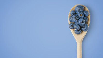 Fresh organic blueberries in wooden spoon isolated on blue background with copy space. Healthy...