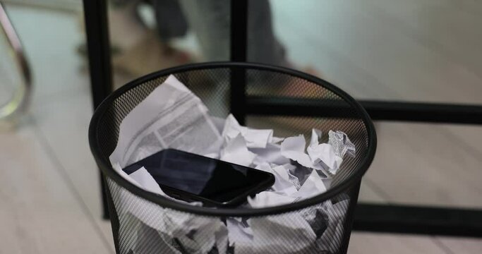 Mobile phone falls into office garbage basket near table