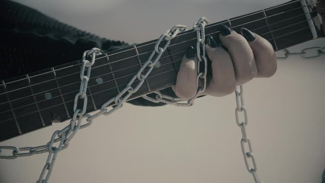 Close up with gothic women playing on scratched guitar with chains in slow motion. Dark nails. Pitch Black. Cold color correction, 4k