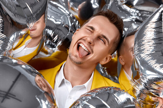 happy winking man in yellow jacket with a lot of silver air balloons. birthday party