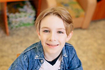 boy 7 years old in the school premises, dressed in a white T-shirt with a blue denim shirt, looks...