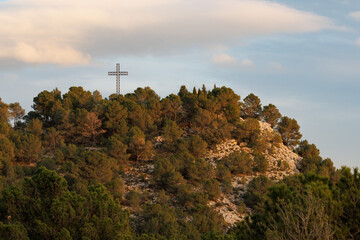 Fototapeta premium Paisaje de la colina de San Cristobal coronando con cruz religiosa metalica en las ultimas luces del día, Alcoy, España
