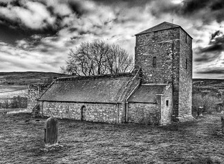 Ancient stone church is situated adjacent to a road on a somber, overcast day