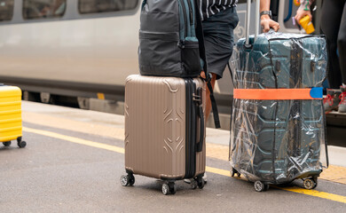 Fototapeta premium Happy loving couple with luggage and backpack walking along railway platform as they are ready to travel on holiday. Man and woman holding hands, looking back and smiling. Travel by train concept