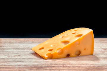 piece of yellow cheese radomer on a wooden board on a black background