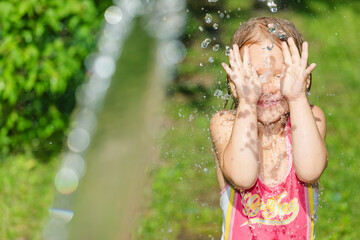Delighted child playing with splashing water in a summer garden