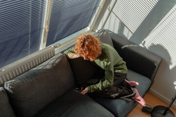young red-haired woman in living room on sofa using phone