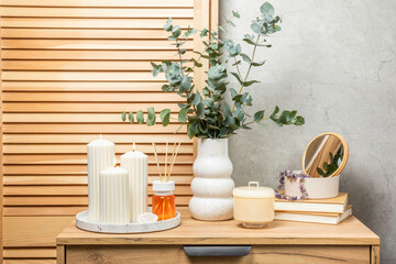 Green eucalyptus leaves in a vase stand on a chest of drawers against the background of a wall. Aromatherapy.Beautiful eucalyptus bouquet.Minimalist interior with flowers, candles and aroma diffuser.
