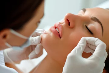 Cercles muraux Salon de beauté Beautiful young woman receiving hyaluronic acid cosmetic injection on her lips in a beauty salon